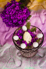 Obraz na płótnie Canvas Bowl with violet flowers and little eggs stands on the blanket