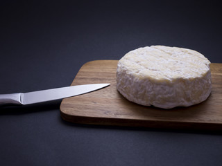 French cow cheese Saint-félicien on wooden cutting board with knife, isolated on black background