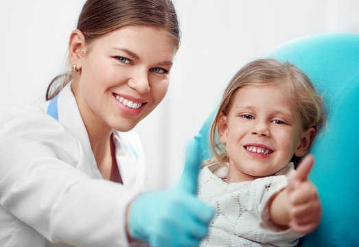 Happy child in dentist chair with female doctor showing thumbs up. 