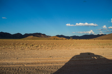 Scenic View of a Desert and Mountain Landscape with Car Shadow near Solitaire, Namibia