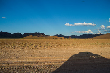 Fototapeta na wymiar Scenic View of a Desert and Mountain Landscape with Car Shadow near Solitaire, Namibia