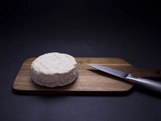 French cow cheese Saint-félicien on wooden cutting board with knife, isolated on black background