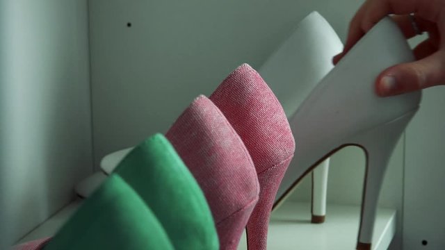 A woman looks at high heel shoes on a shelf - closeup on the shoes and the hand