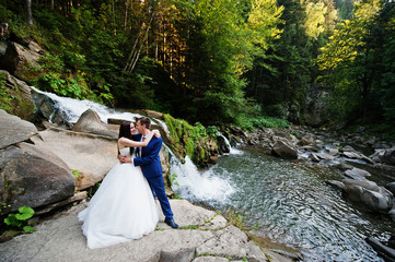 Lovely wedding couple against waterfall on sunset at Carpathian mountains.