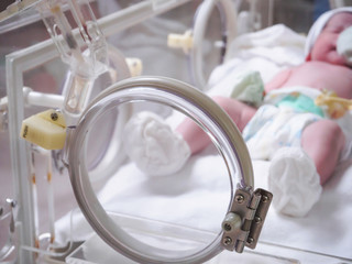Fototapeta na wymiar Newborn baby girl inside incubator in hospital post delivery room