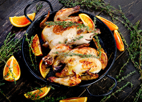 Roasted two chicken with oranges and thyme on a dark wooden background.