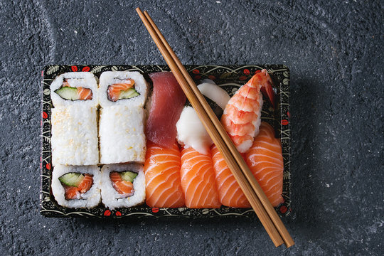 Sushi Set nigiri and sushi rolls in plastic food delivery box with chopsticks over black stone texture background. Top view with space. Japan menu