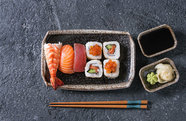 Sushi Set nigiri and sushi rolls in dark ceramic plate with soy sauce and chopsticks over black stone texture background. Top view with space. Japan menu