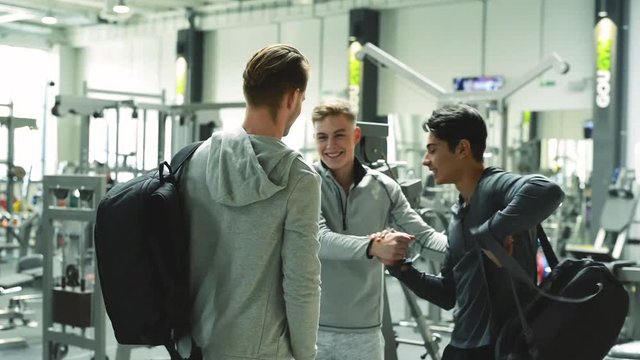Three young fit men in gym greeting each other.