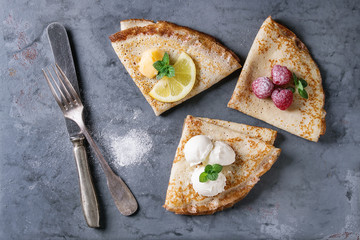 Sweet crepes pancakes with different fillings fresh raspberries, lemon curd, mascarpone cheese, mint, sugar powder with vintage cutlery over gray blue metal texture background. Top view with space