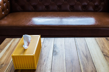 Yellow tissue box on wooden table with luxury sofa.