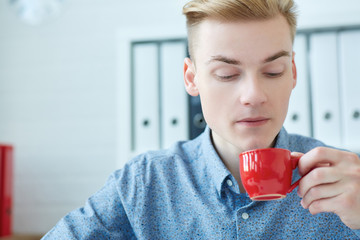 Young businessman blowing a hot cup of coffee in office.