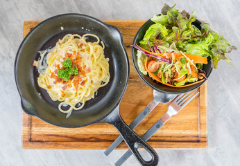 Lunch set, pasta in creamy sauce and vegetable salad are in black ceramic ware serve on rustic wood tray.