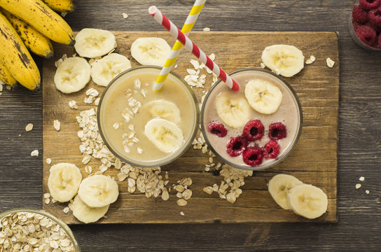 Useful and delicious smoothies. Banana with oatmeal and raspberry with banana and oatmeal on a wooden board on a black wooden background, top view