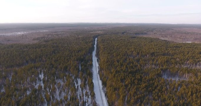 Siberia, 2017: Aerial view of beautiful winter landscape from a bird's eye view: a winter coniferous forest and a road in the middle. A rural desert road surrounded by a winter forest with a copter.