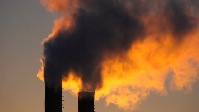 Harmful emissions from the plant pipe against the background of the setting sun
