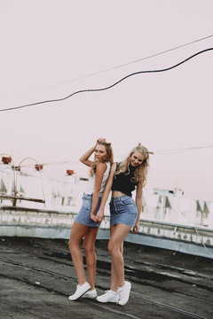 lifestyle and people concept: Fashion portrait of two stylish girls best friends wearing jeans skirts, outdoors on the roof. Happy summer time for fun.