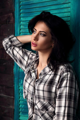 Fototapeta premium Beautiful makeup woman in trendy black and white checkered shirt thinking on blue wooden background. Short hairstyle