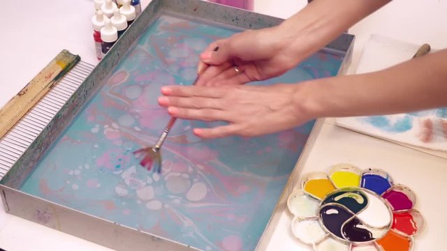 An artist dropping paint into the water creating ebru picture slow motion