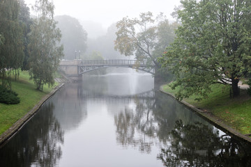 Obraz premium Park with a canal foggy morning. Through the mist visible bridge over the canal.