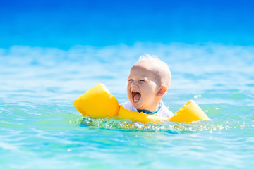 Baby swimming in ocean water on tropical beach