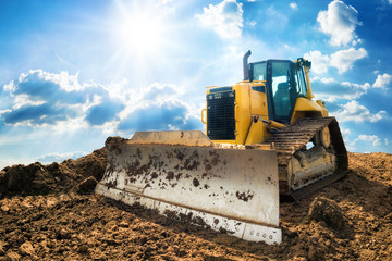 Yellow excavator on new construction site, with the bright sun and nice blue sky in the background  - obrazy, fototapety, plakaty