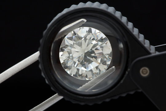 loose brilliant round diamonds is being held by tweezers and looked through a black loupe