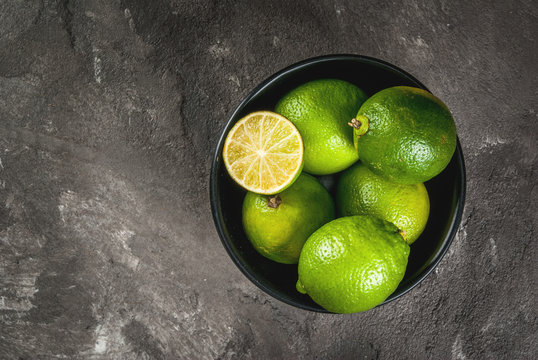 Fresh organic tropical citrus fruits lime in a black bowl on a gray concrete background. Whole and half. Copy space top view