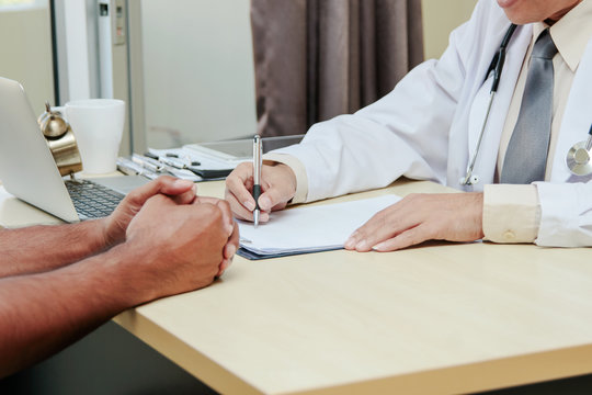 Asian doctor talking and taking notes with male patient (consultation)