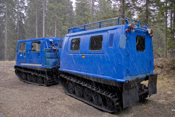 small snowcat with second wagon attached to the trailer coupling, electric blue, used to transport people in mountain huts, photographed in early spring, during snowfall, Trentino Alto Adige,  Italia