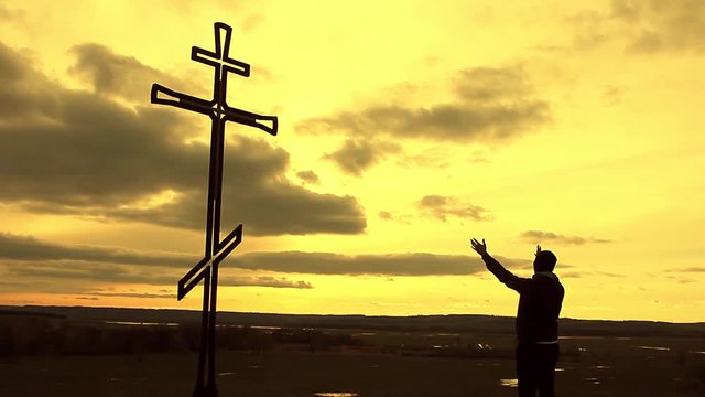 Silhouette man on top of the mountain looking with hope at the Christian Cross. A man making a confession to the cross, background sunset.