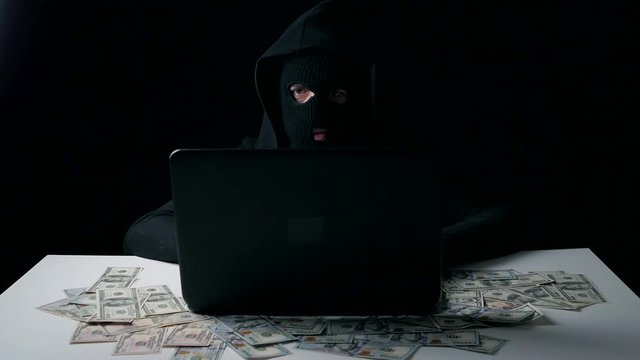 A hacker in a balaclava earns money. Cyber crime. - Powered by Adobe