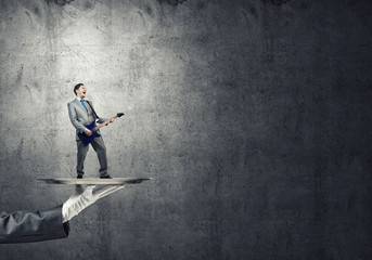 Businessman on metal tray playing electric guitar against concrete background