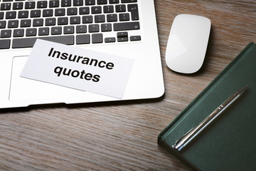 Card with text INSURANCE QUOTES and laptop on wooden background