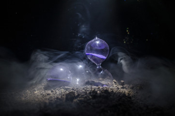 Naklejka premium Time concept. Silhouette of Hourglass clock and smoke on dark background with hot yellow orange lighting, or symbols of time with copy space, sandglass or sand clock