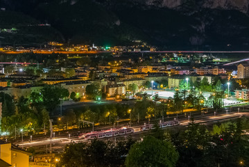 Fototapeta premium Sustainable city, colorful lights and traffic at night in mountain valley, Trento, Italy