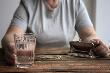 Fototapeta na wymiar Senior woman sitting at table with glass of water, purse and coins, closeup. Poverty concept