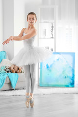 Young beautiful ballerina dancing in room