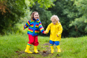 Fototapeta premium Kids play in rain and puddle in autumn