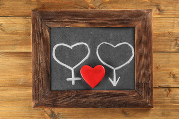 Blackboard with drawn gender symbols and red heart on wooden background