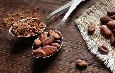 Spoons with aromatic cocoa beans and powder on wooden table