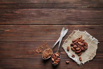 Spoons with aromatic cocoa beans and powder on wooden table