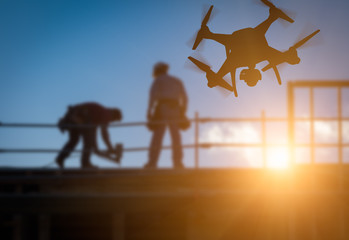Silhouette of Unmanned Aircraft System (UAV) Quadcopter Drone In The Air Over Building Under...