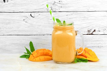 Tropical mango coconut smoothie in a mason jar glass, on a rustic white wood background