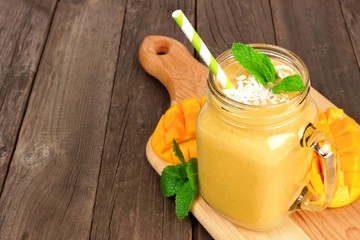 Mango coconut smoothie in a mason jar glass on paddle board against a rustic wood background