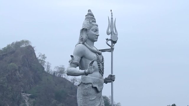 A side shot of a large statue of the Hindu god Shiva looking over the ghats of Haridwar