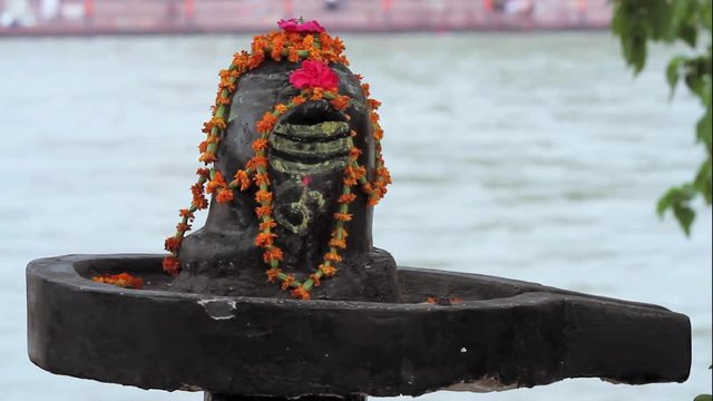 A close up shot of a Shiva-lingam, the generative symbol of the Hindu god Shiva with the Ganges River flowing in the background