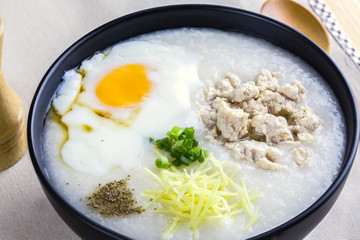 Rice porridge is topping with ginger, spring onion, pepper, chicken, and onsen egg, Breakfast set on wooden table, spoon, pepper grinder. breakfast in Asia call 