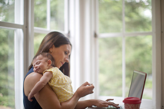 newborn smiles in sleep while mother works in home office
