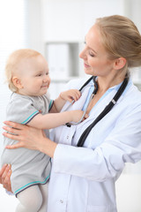 Pediatrician is taking care of patient in hospital. Female doctor holds toddler girl at hands. Health care, insurance and help concept.